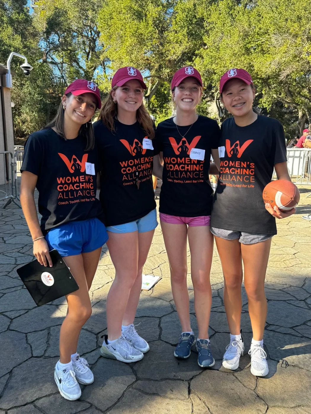 Four young women coaches in Women’s Coaching Alliance shirts and Stanford caps